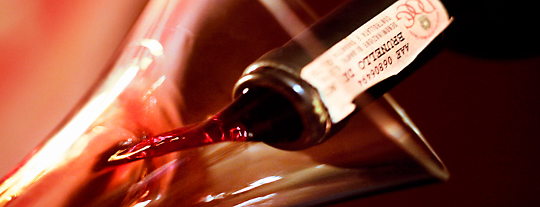talien, Toskana, Rotwein: Ausschank von Brunello aus der Flasche in einen Dekander, zu sehen sind Flaschenhals mit Ettikett und Öffnung des Dekanders, warme Rottöne und sanftes Licht dominieren das Foto